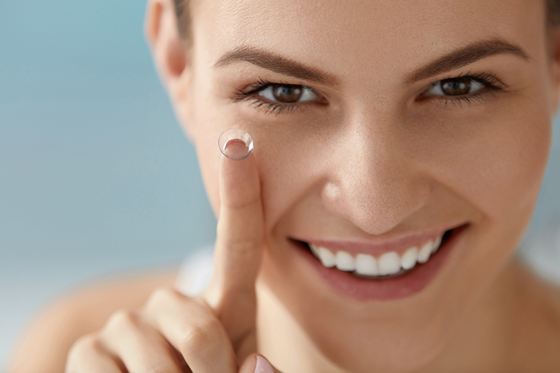 Smiling woman with contact lens on her finger close up.